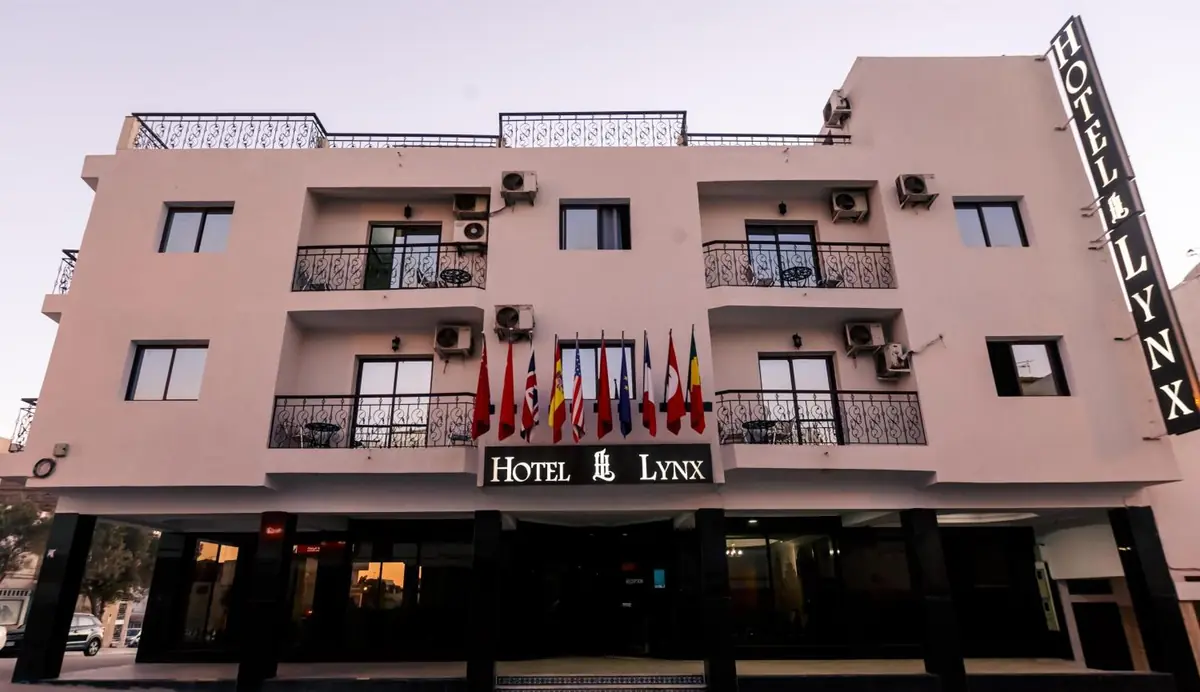 The front of Hôtel Lynx in Talborjt: a three-storey pink building with wrought-iron balconies, a row of flags and the black HOTEL LYNX sign above the entrance.