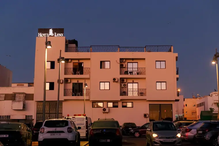 Hôtel Lynx at blue hour seen from across the street: the lit HOTEL LYNX rooftop sign, street lamps and cars parked in front.