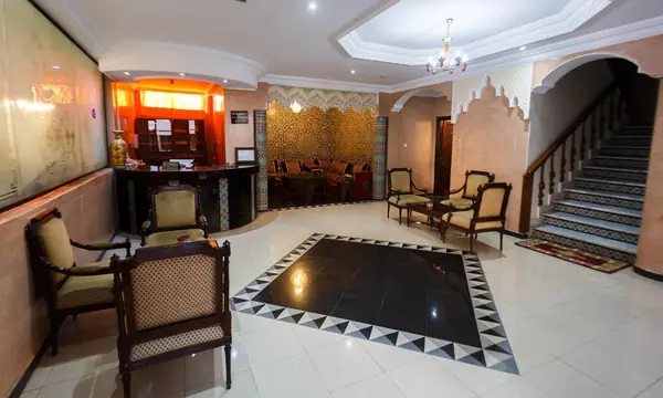 The reception of Hôtel Lynx: a lit wooden desk, carved chairs, a marble floor and the staircase with blue-tiled steps.