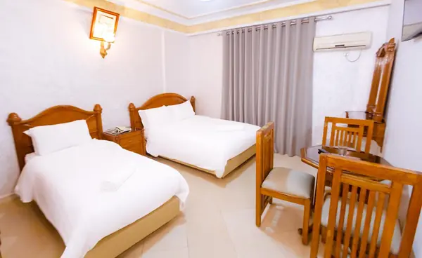 Triple room at Hôtel Lynx: a single bed and a large double bed, table and chairs, grey curtains and a wall TV.
