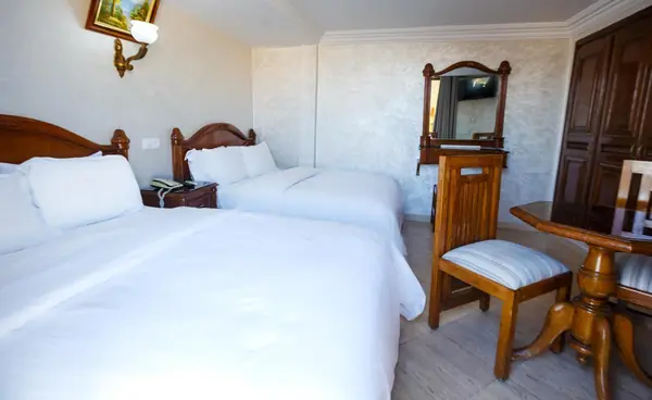 A Triple at Hôtel Lynx with a double and a single bed, a wooden dressing table with mirror and a table with chairs.
