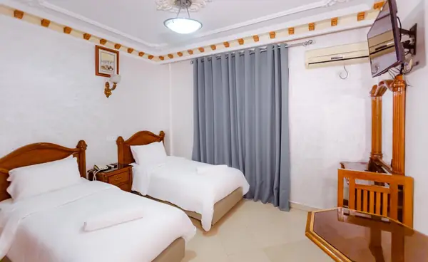 Twin room at Hôtel Lynx: two single beds with white linen, grey curtains, a wall-mounted TV and air-conditioning unit.