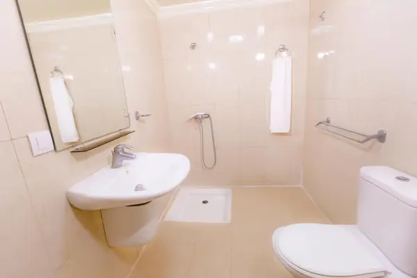 Shower room at Hôtel Lynx: a wall basin under a mirror, a towel rail, an open walk-in shower and a toilet on cream tiles.