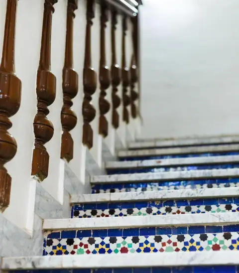 The staircase of Hôtel Lynx: carved wooden balusters and steps with blue, red and yellow zellige tiles.